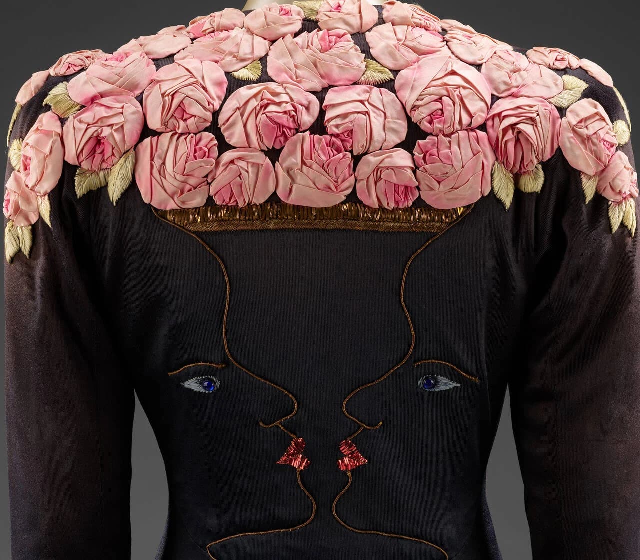 Black Schiaparelli coat with embroidered faces and a collar of pink roses, from Fashion Becomes Art.