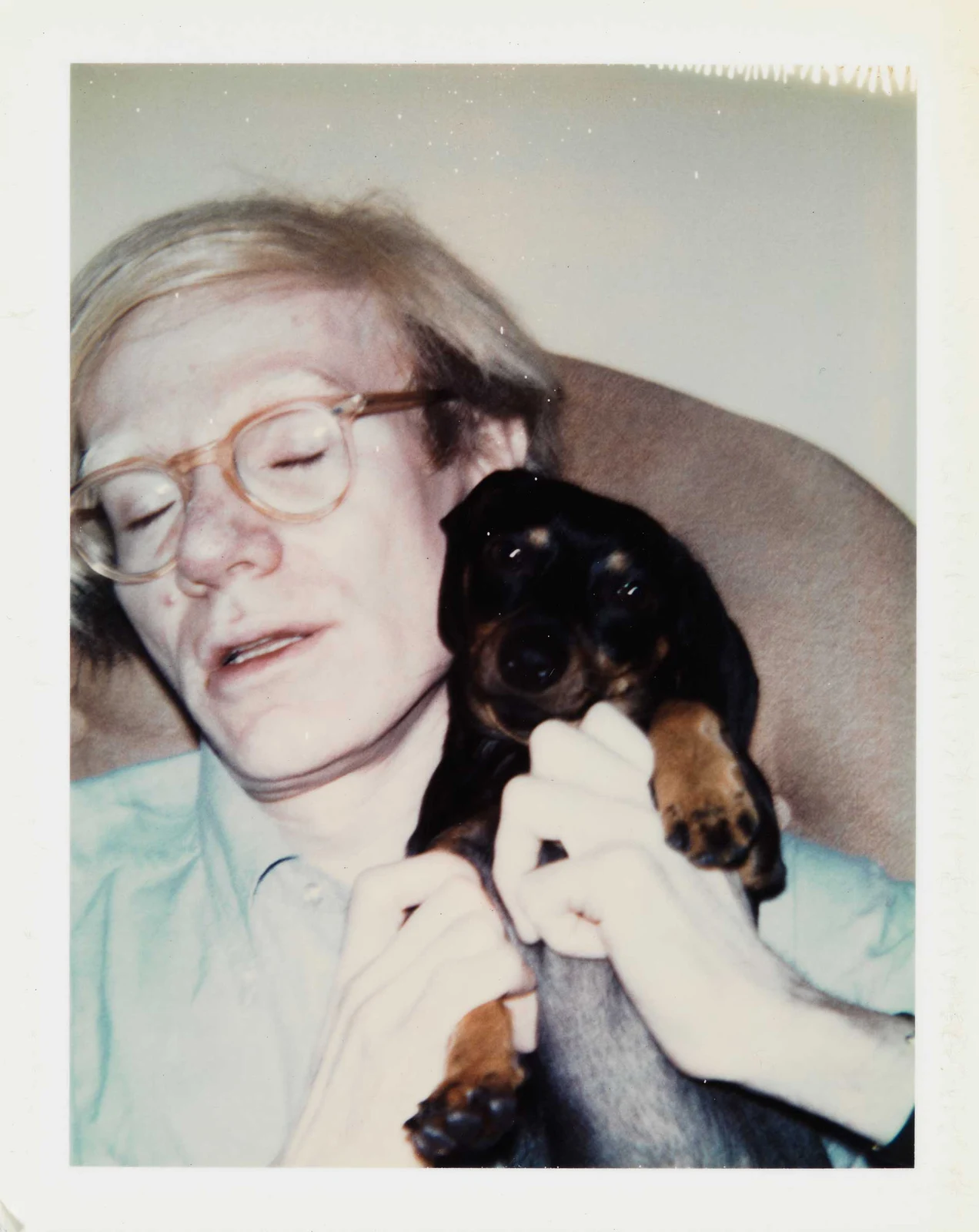 Andy Warhol holding a small dog in a Polaroid, the official image for Andy Warhol Family Album.