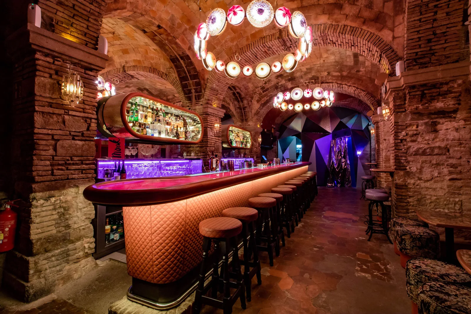 A curved cocktail bar beneath brick arches at Monk