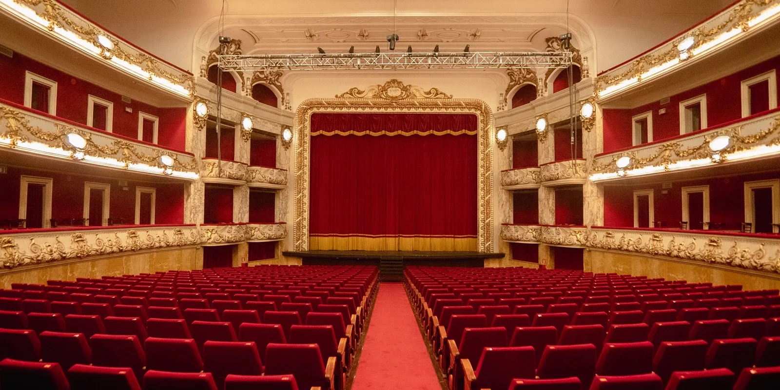 Red seats facing a curtained stage beneath ornate balconies at Teatre Tívoli