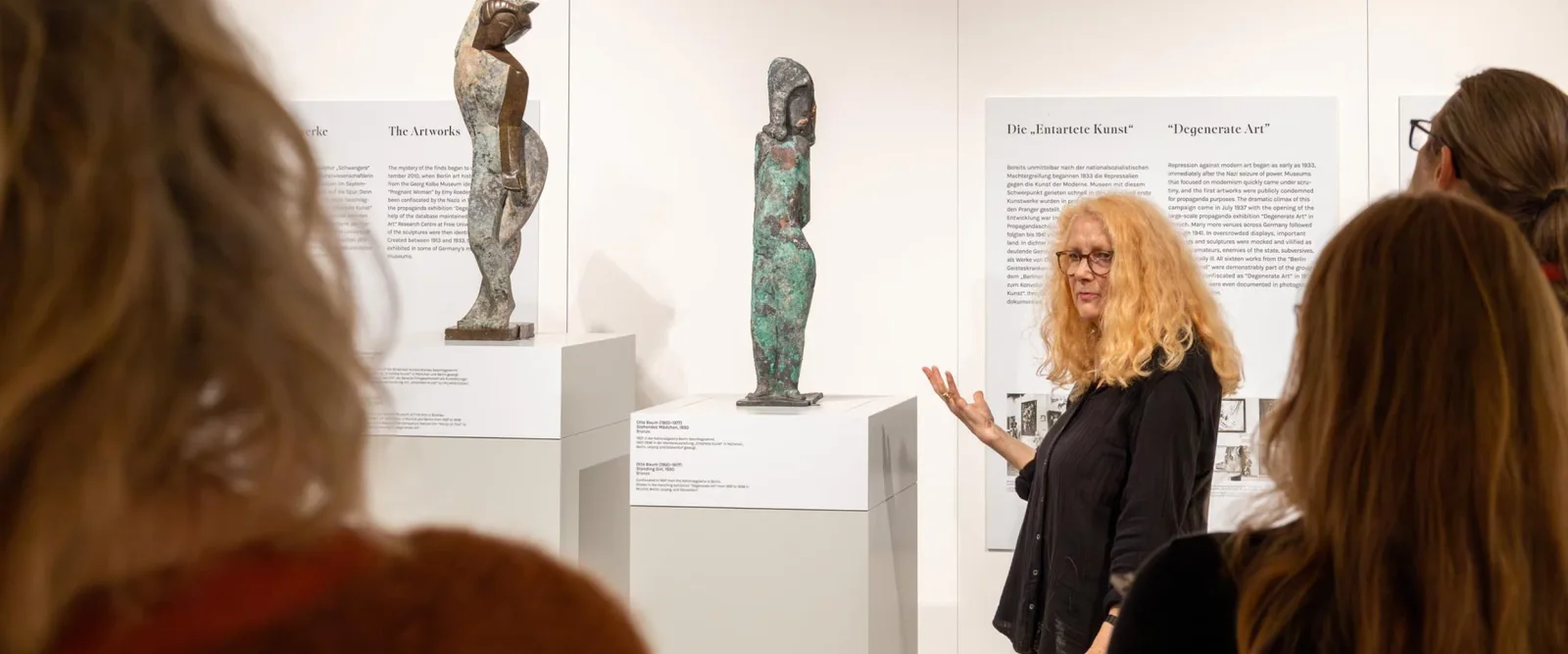 Petri Berlin: visitors listening to a guide beside displayed sculptures, pictured by the listed source