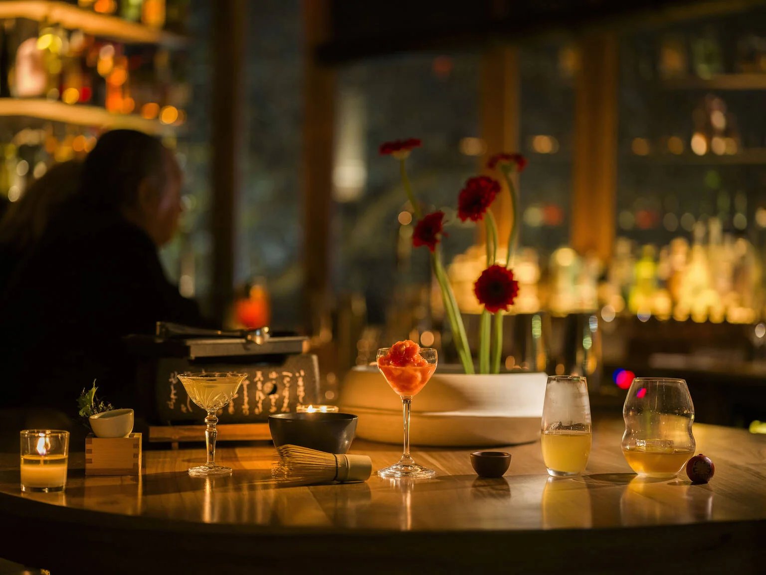 Kōnā Corner: cocktails and flowers arranged on the softly lit bar