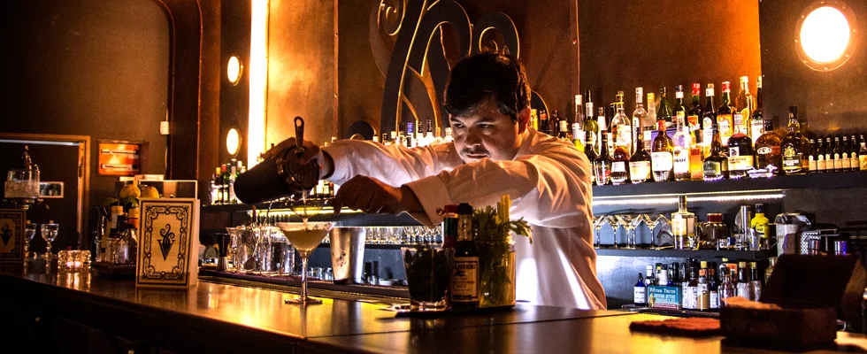 A bartender pouring a drink beneath warm pendant lights at Verne Club