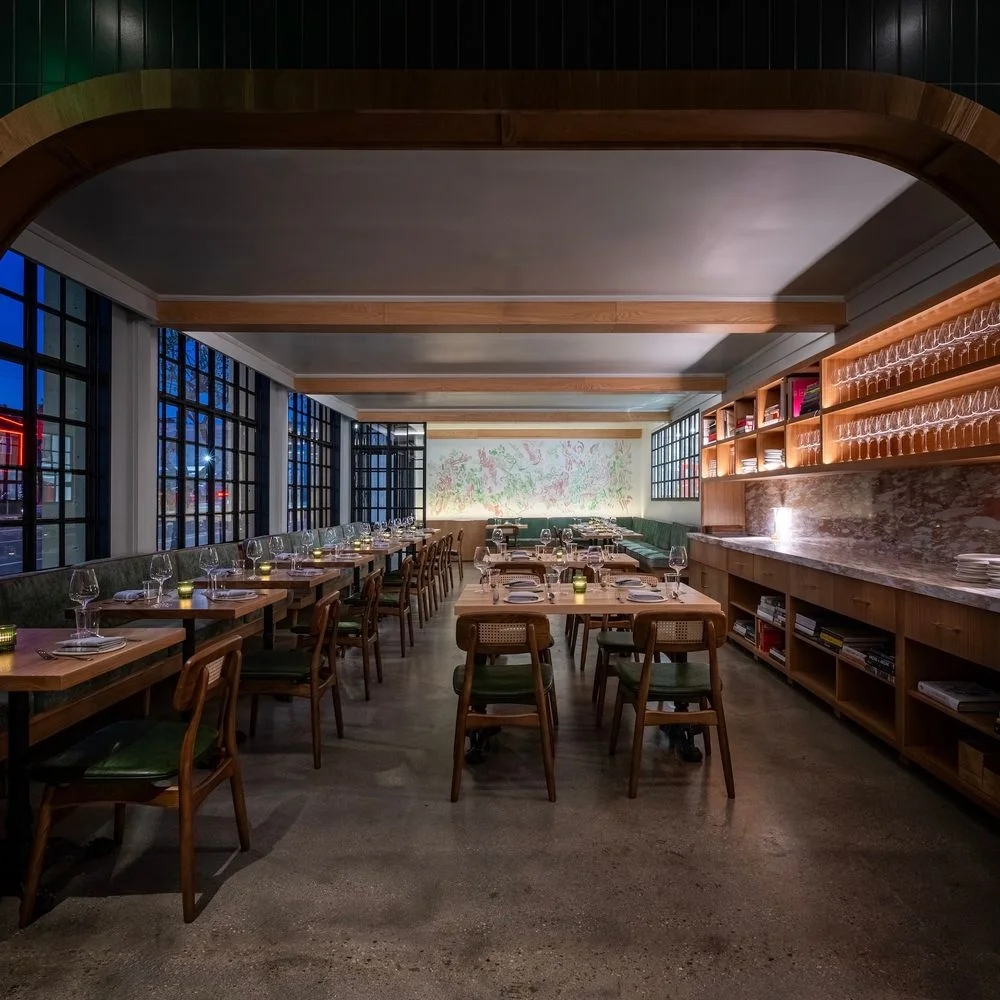 Wooden tables between tall windows and illuminated shelves at Firstborn