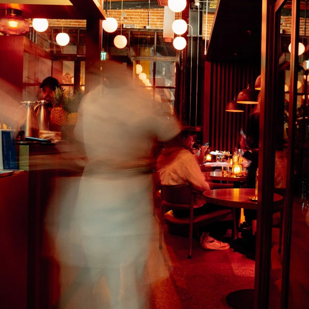 A warmly lit dining room with guests and a passing server at Lynx