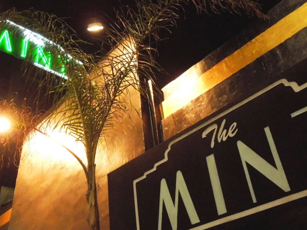 The Mint: the venue's illuminated name sign beside a palm tree at night
