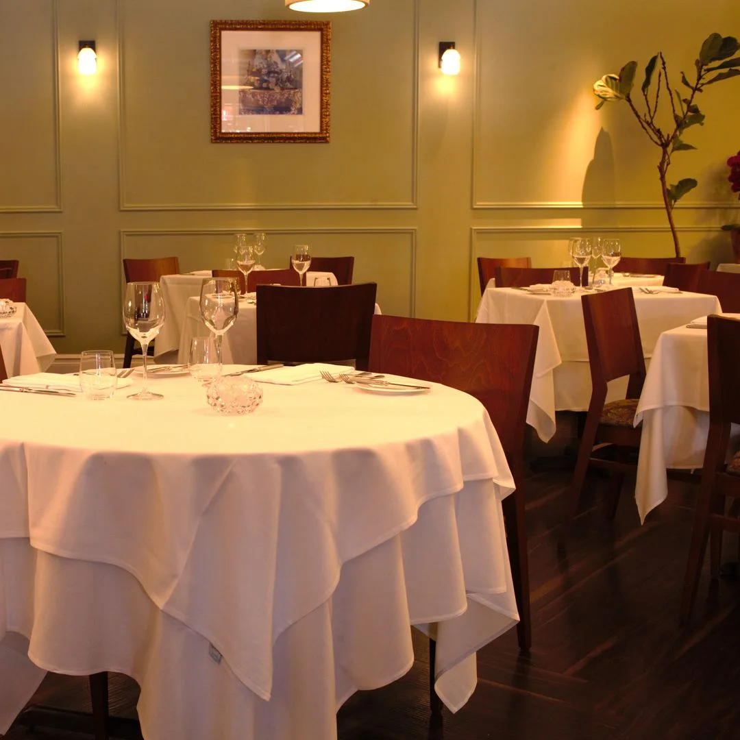 White-clothed round tables beneath warm wall lights at Eulalie