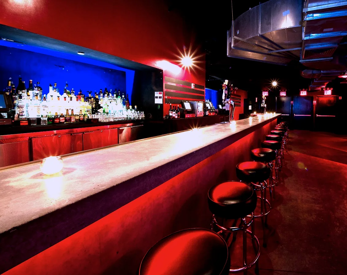 A long red-lit bar with round stools at Le Poisson Rouge