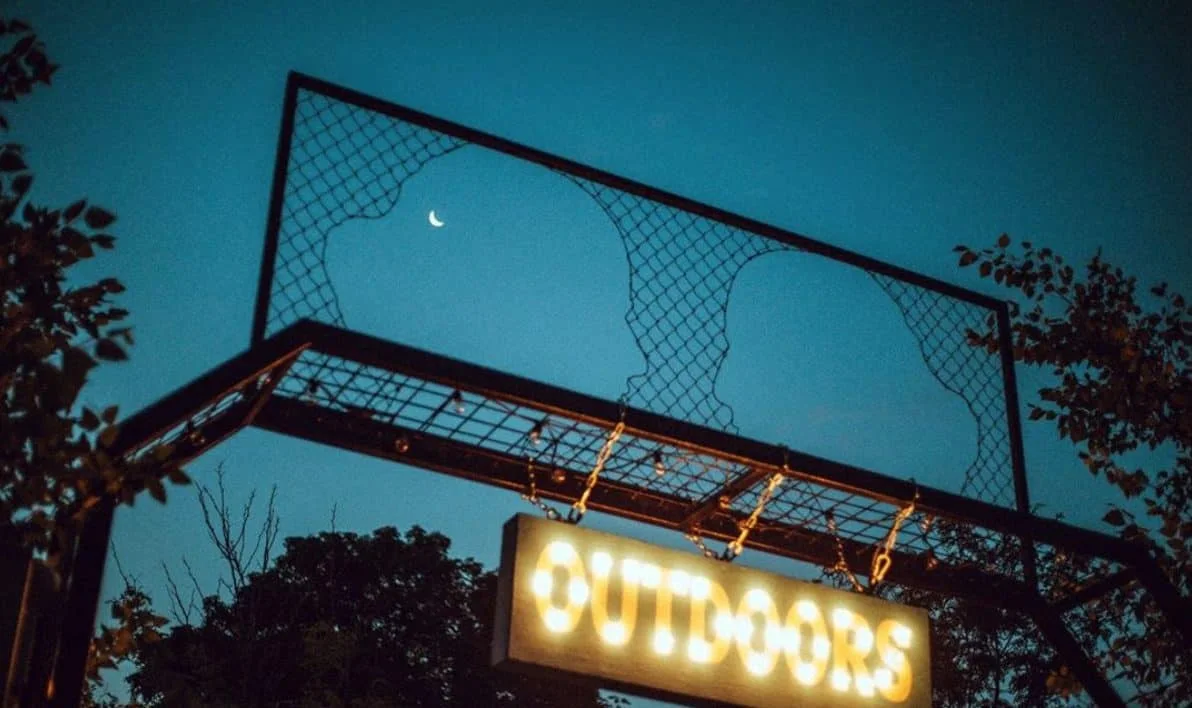 An illuminated outdoor sign beneath a night sky at Nowadays