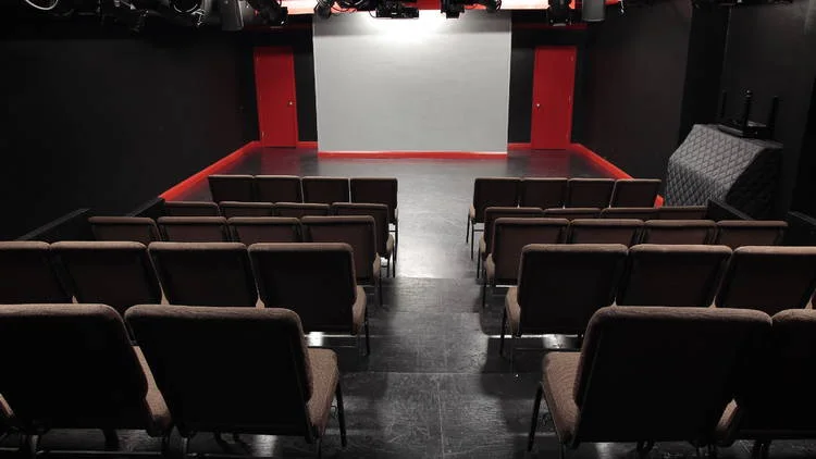 Rows of seats facing a small black-box stage at The PIT Loft