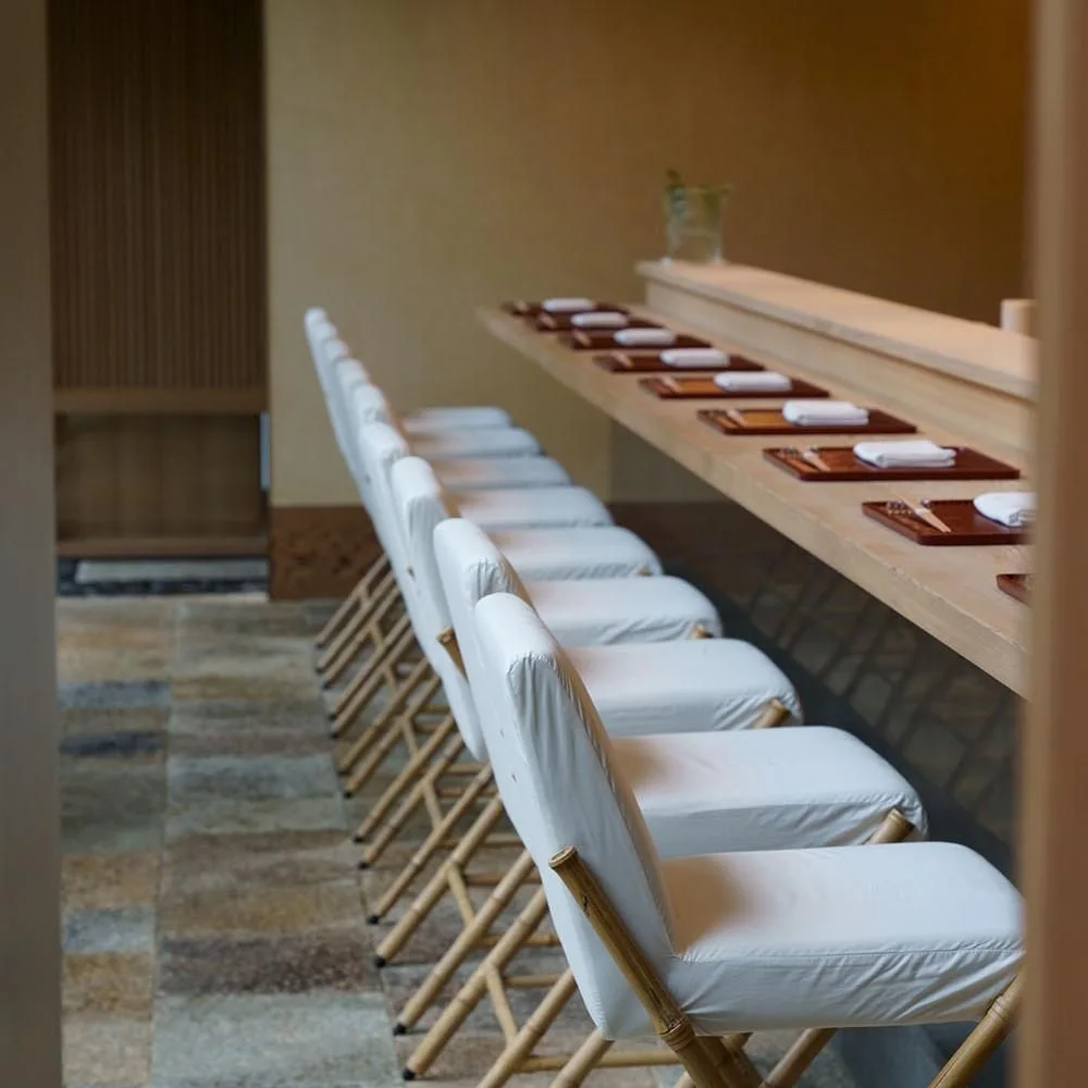 A long wooden counter lined with white upholstered seats at Kanda