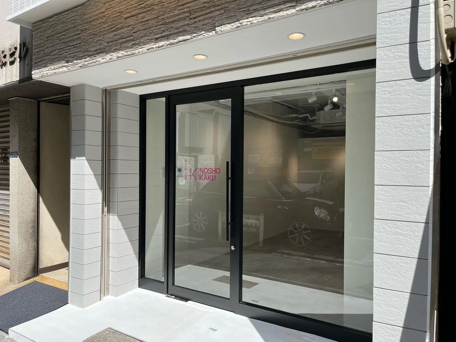 Kinosho Kikaku: street-level gallery entrance with black-framed glass doors and a pale tiled facade