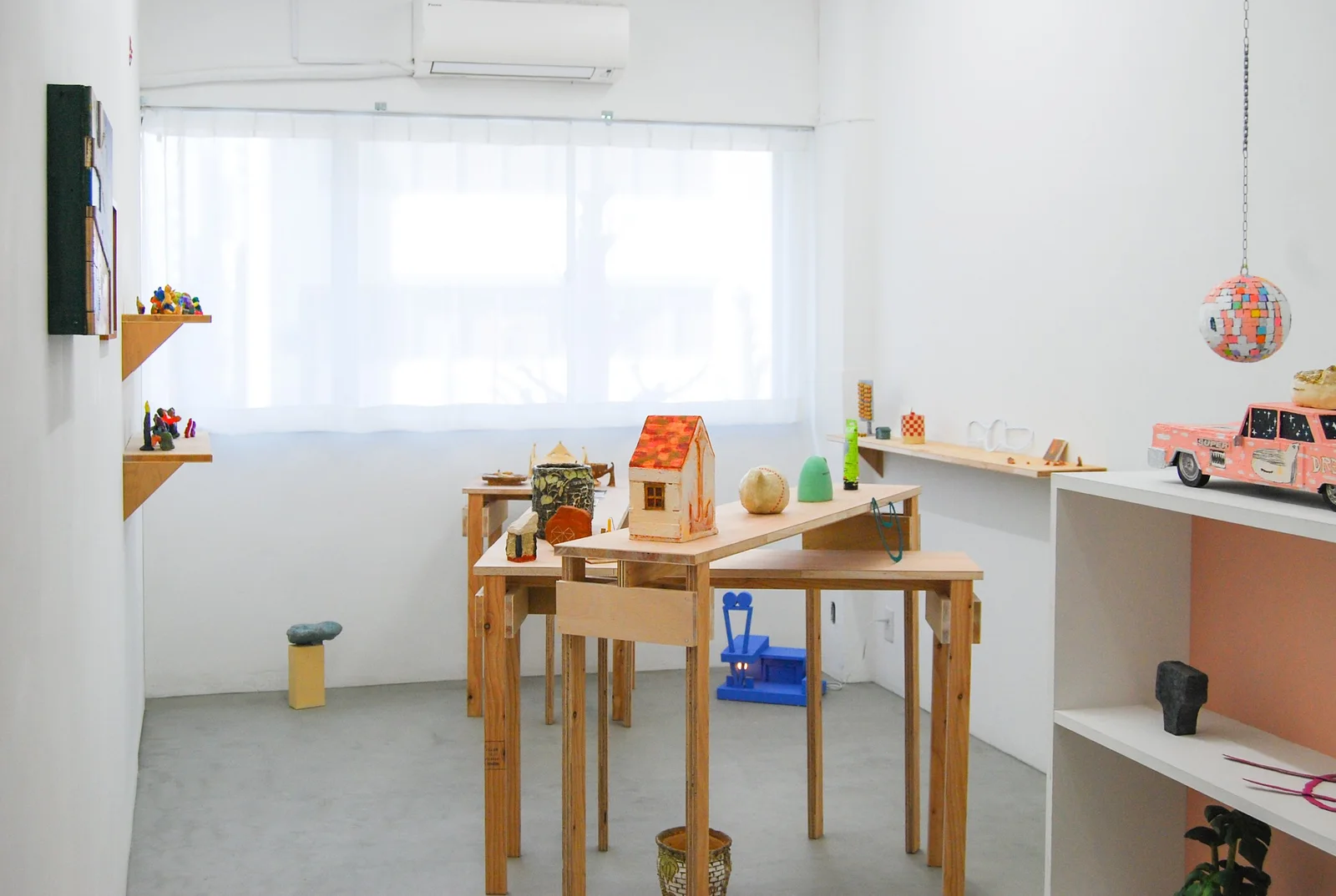 Kohtoh: daylit gallery with shelves and wooden tables displaying small artworks and ceramic objects