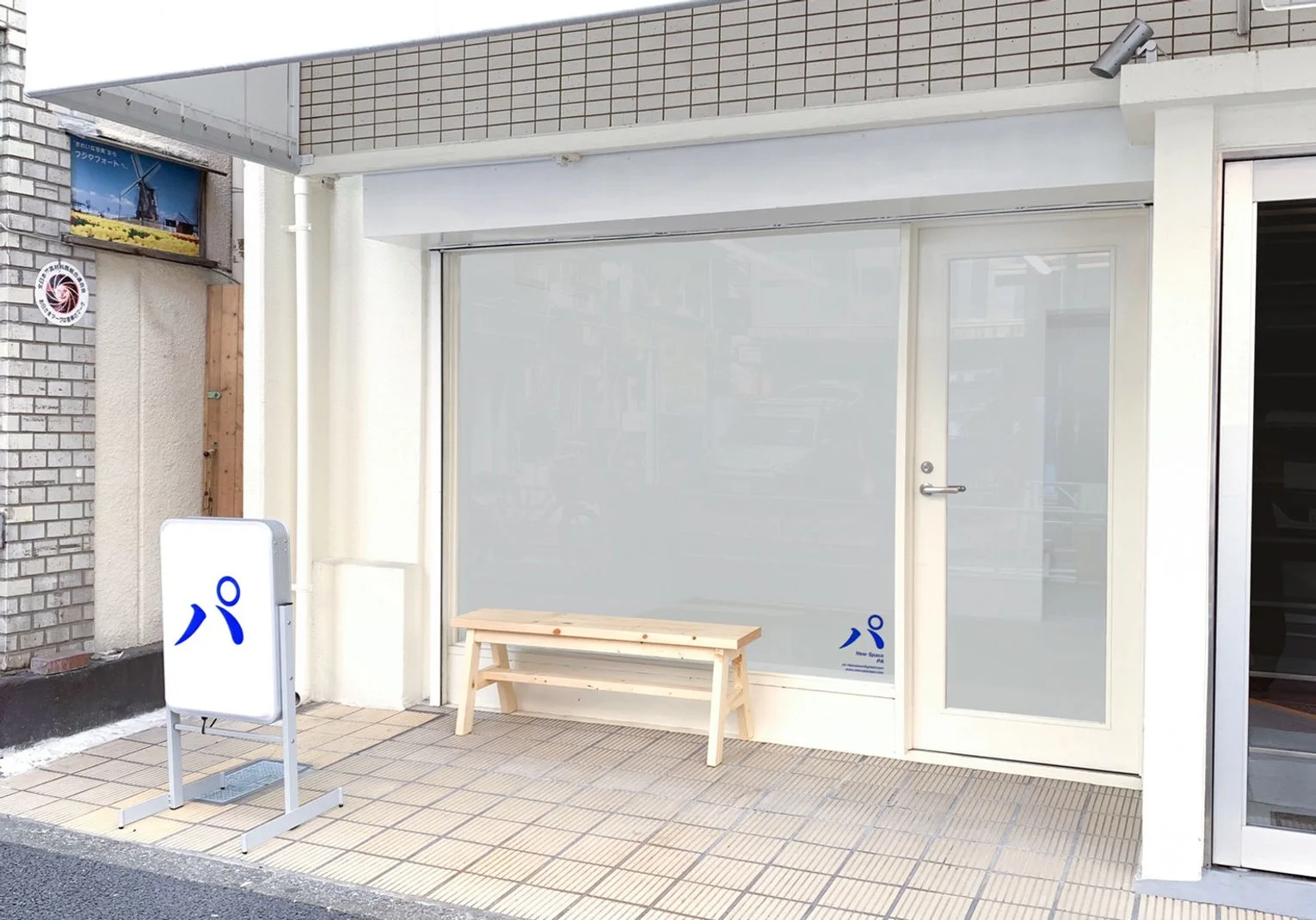 The gallery's white street entrance and small bench at New Space PA