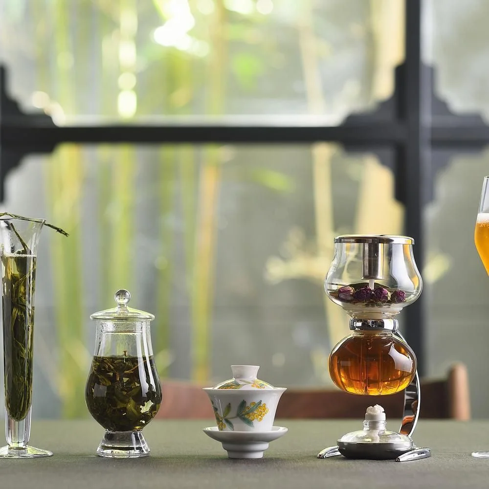Tea vessels arranged on a table beside a leafy window at Sazenka